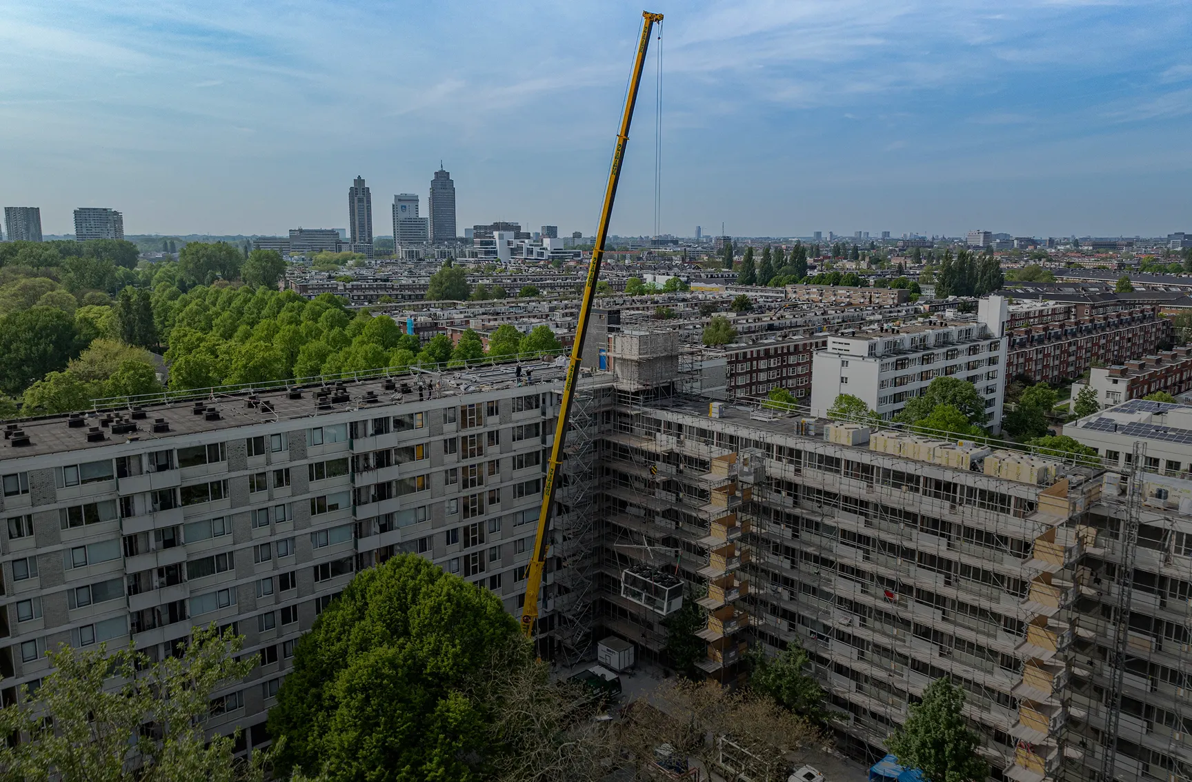 Warmtepompen worden met een kraan op het dak van een Amsterdamse flat gehesen